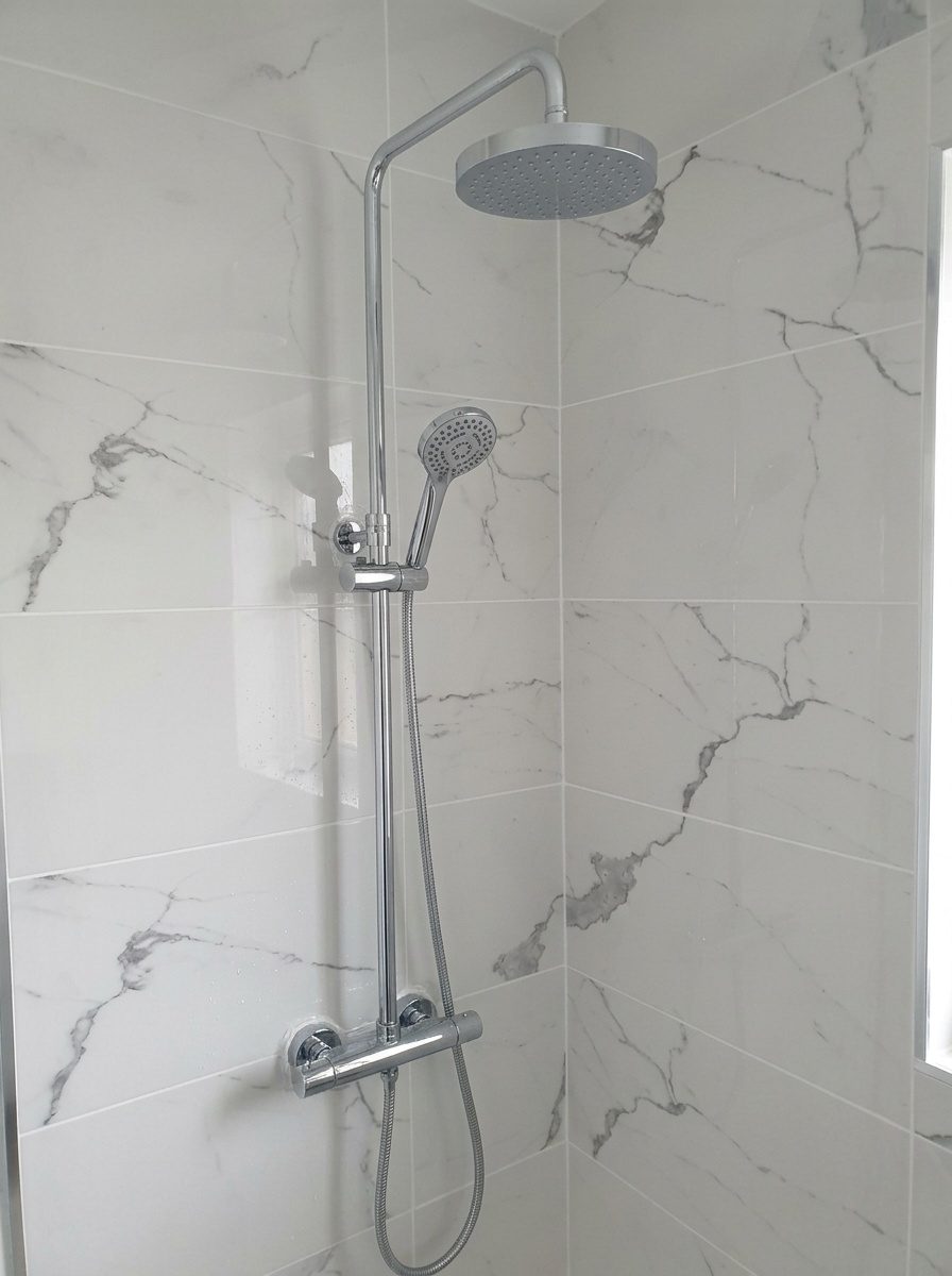 Plombier réglant le mitigeur thermostatique d'une colonne de douche après la pose
